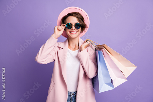 Photo of sweet pretty optimistic bob hair young woman carry shop bags wear glasses pink cap coat isolated on purple color background