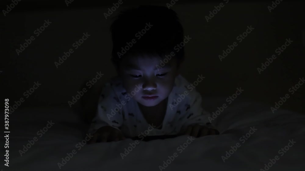 Asian child lying on bed and playing on mobile phone Asian child lying on bed and playing on mobile phone