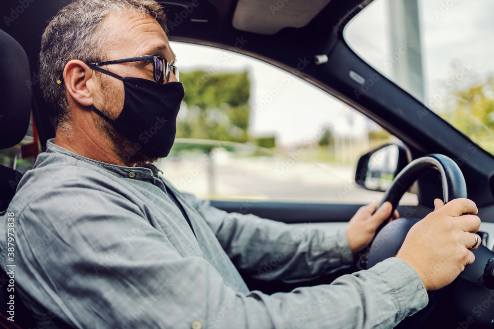 Middle aged man with eyeglasses, with protective face mask on sitting in his car and driving it during corona virus outbreak. Middle aged man with eyeglasses, with protective face mask on sitting in his car and driving it during corona virus outbreak.