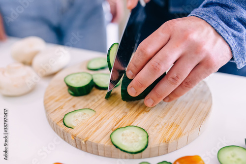 Couple cooking together in the kitchen at home. Close-up of a man's hands slicing a cucumber.