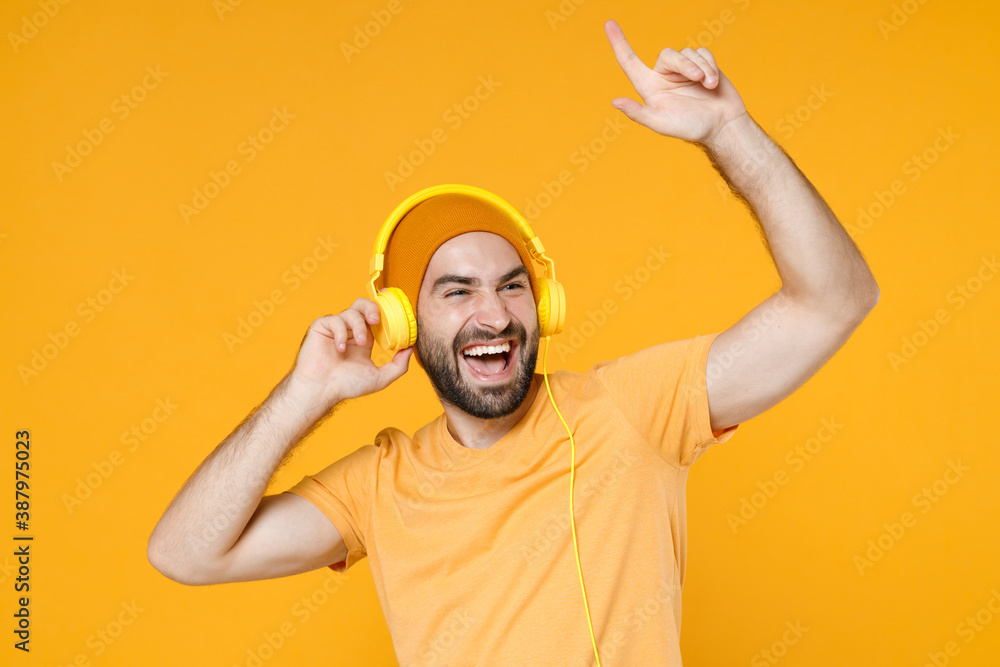 Laughing young bearded man wearing basic casual t-shirt hat listening music  with headphones dancing pointing index finger up looking aside isolated on  bright yellow colour background, studio portrait. Stock Photo | Adobe