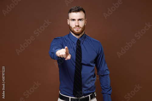 Displeased strict bearded young business man wearing blue shirt tie pointing index finger on camera isolated on brown colour background studio portrait. Achievement career wealth business concept.