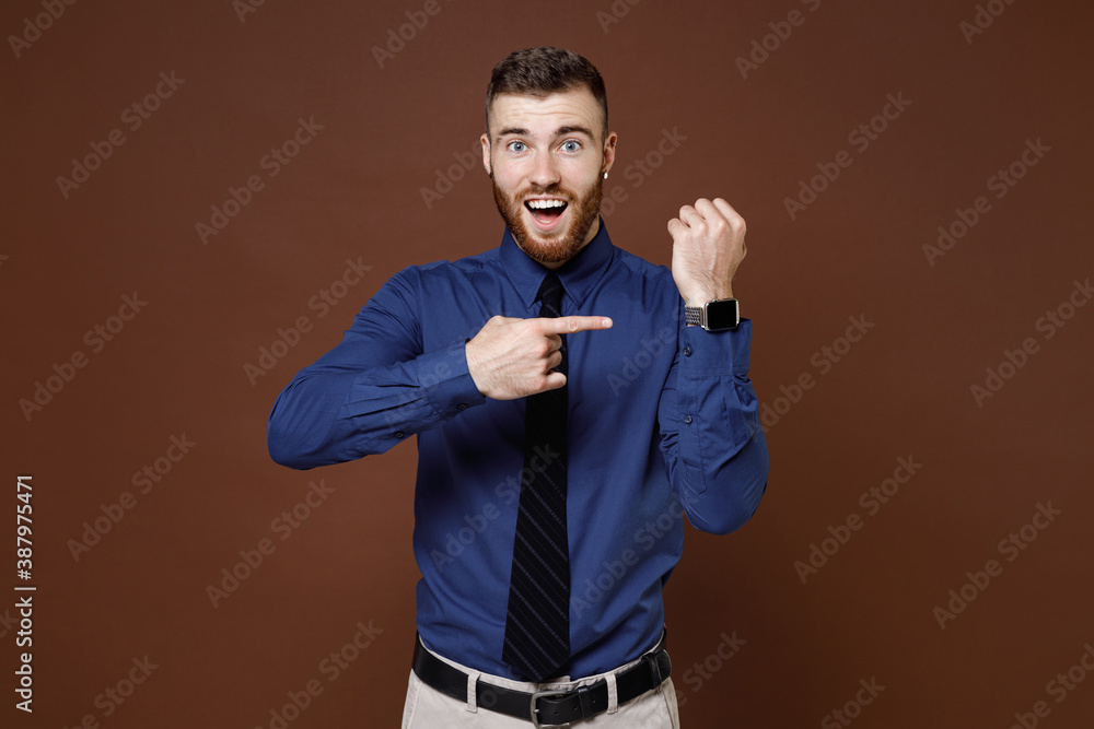 Excited shocked bearded young business man wearing blue shirt tie pointing index finger on smart watch on hand isolated on brown background studio portrait. Achievement career wealth business concept. Excited shocked bearded young business man wearing blue shirt tie pointing index finger on smart watch on hand isolated on brown background studio portrait. Achievement career wealth business concept.