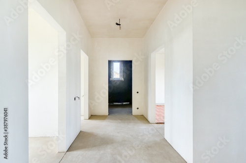 The unfinished clean hallway under construction without decoration with the white plastered walls in new building