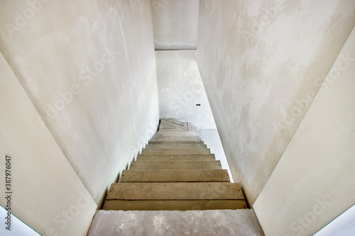 The top view the unfinished wooden staircase leading down to the basement in a new residential building with the white plastered walls