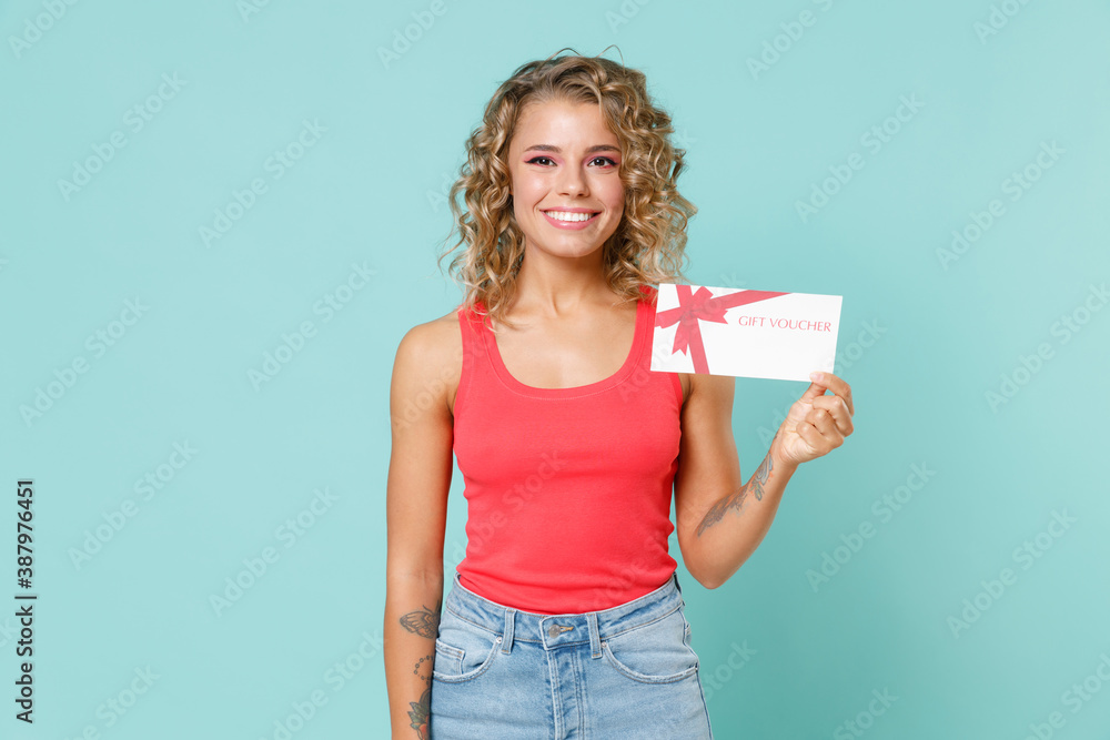 Smiling beautiful attractive young blonde woman wearing pink basic casual tank top standing hold in hand gift certificate looking camera isolated on blue turquoise colour background studio portrait. Smiling beautiful attractive young blonde woman wearing pink basic casual tank top standing hold in hand gift certificate looking camera isolated on blue turquoise colour background studio portrait.