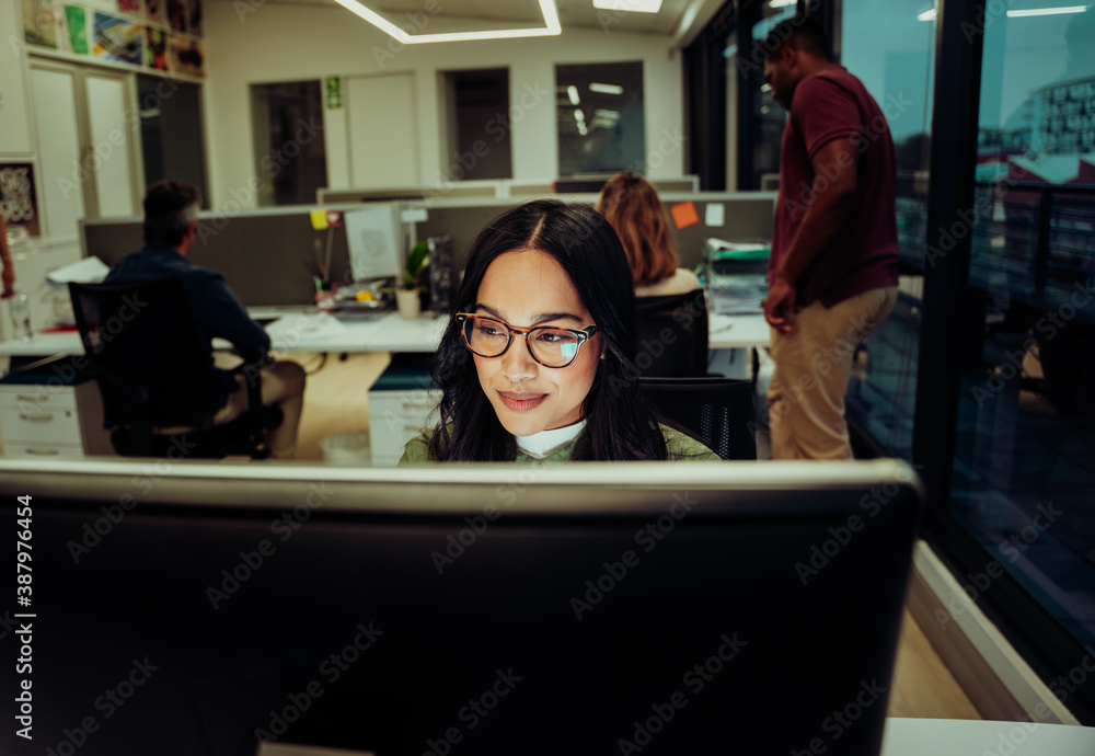 Multi-ethnic business women typing on desktop working on design report while colleagues work on collaboration project Multi-ethnic business women typing on desktop working on design report while colleagues work on collaboration project