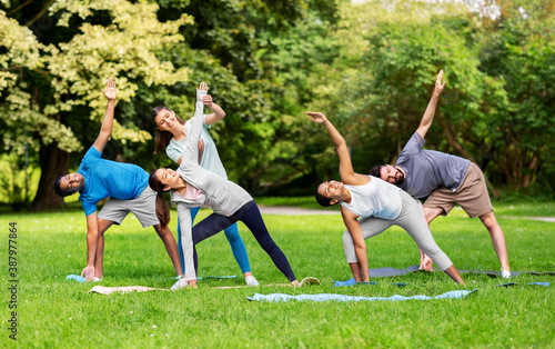 fitness, sport and healthy lifestyle concept - group of happy people doing yoga with coach at summer park