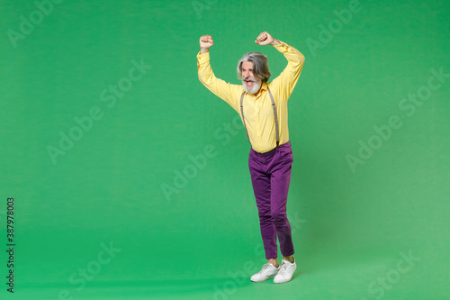 Full length of screaming elderly gray-haired mustache bearded man wearing casual yellow shirt suspenders expressive gesticulating with hands isolated on bright green colour background studio portrait.