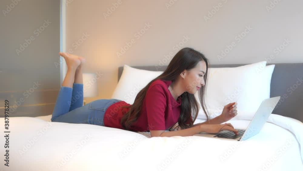 In a well-appointed hotel suite, and while lying on the bed on her stomach, a pretty young woman enters her credit card into the laptop.