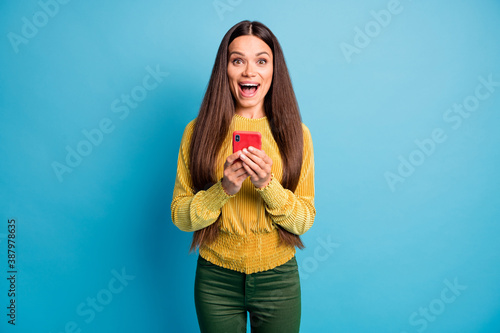 Photo portrait of surprised woman with open mouth holding phone in two hands isolated on pastel blue colored background