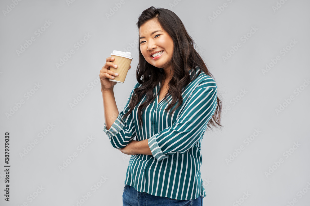 people and drinks concept - happy young asian woman drinking takeaway coffee from paper cup over grey background people and drinks concept - happy young asian woman drinking takeaway coffee from paper cup over grey background