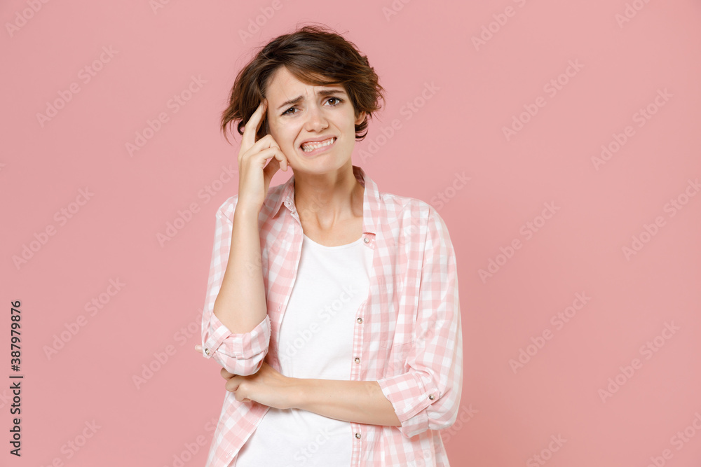 Preoccupied concerned puzzled confused young brunette woman 20s in casual basic checkered shirt standing put hand on head looking camera isolated on pastel pink colour background, studio portrait. Preoccupied concerned puzzled confused young brunette woman 20s in casual basic checkered shirt standing put hand on head looking camera isolated on pastel pink colour background, studio portrait.