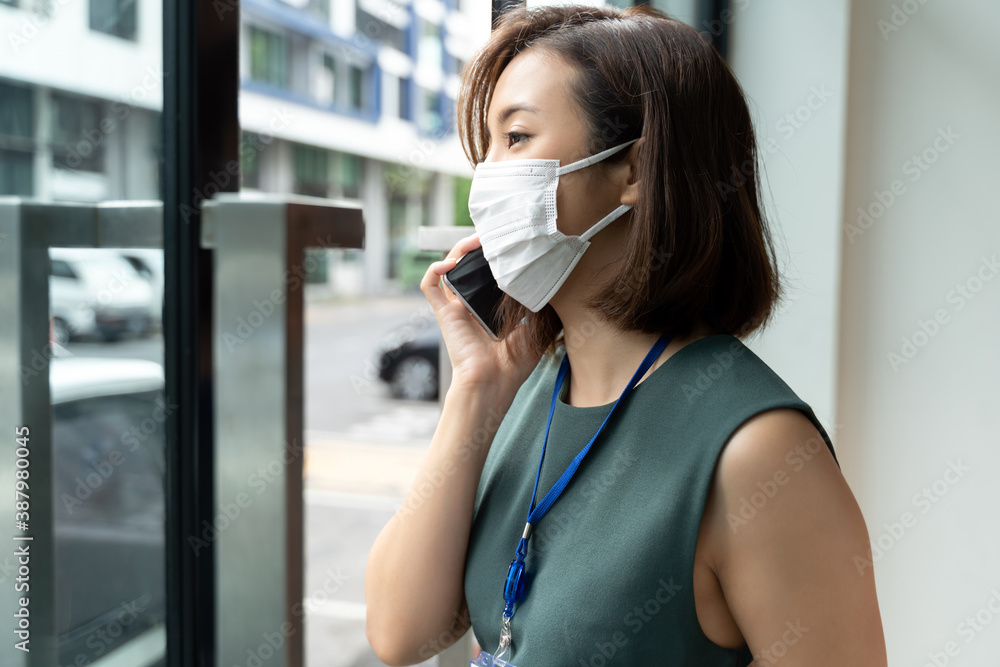 Portrait Asian business woman wearing hygienic mask talking on the phone outside office.
