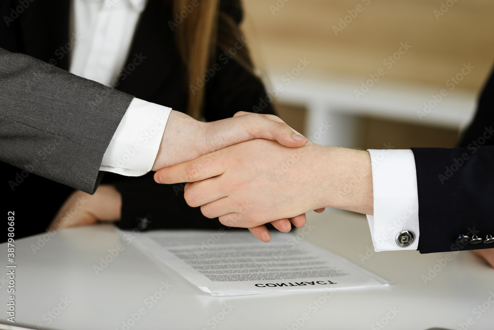 Unknown businessman shaking hands with his colleague or partner above the glass desk in modern office, close-up. Business people group at meeting Unknown businessman shaking hands with his colleague or partner above the glass desk in modern office, close-up. Business people group at meeting