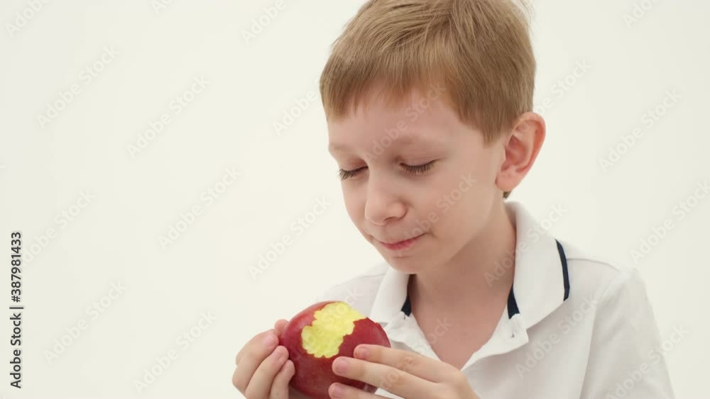 Little boy in white polo missing some teeth eats red apple on the light background. Slow motion Little boy in white polo missing some teeth eats red apple on the light background. Slow motion