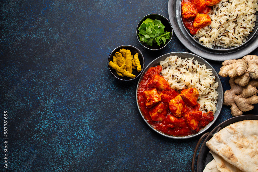 Chicken tikka masala dish with rice, flat Indian bread and spices in rustic metal plates on concrete background top view. Chicken tomato curry, traditional Indian meal, free space for text