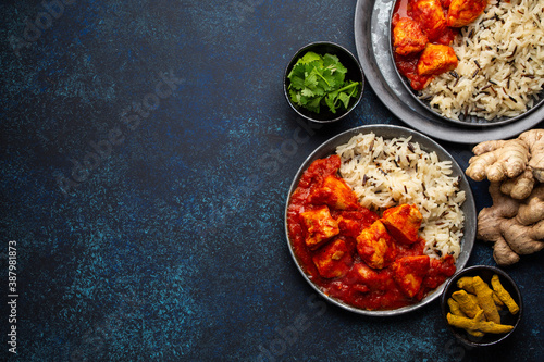 Chicken tikka masala dish with rice, flat Indian bread and spices in rustic metal plates on concrete background top view. Chicken tomato curry, traditional Indian meal, free space for text