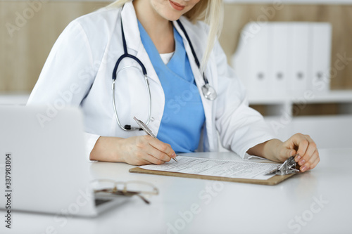 Unknown woman-doctor at work filling up medication history record form in clinic, close-up of clipboard
