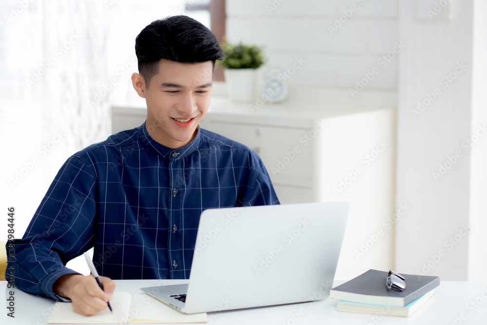 Young asian business man writing on notebook for planning working and using laptop computer on desk at home, notes about finance, male study and learning, business and communication concept. Young asian business man writing on notebook for planning working and using laptop computer on desk at home, notes about finance, male study and learning, business and communication concept.