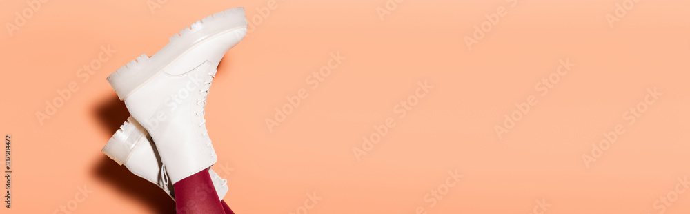 cropped view of female legs in red tights and white boots on peach background - obrazy, fototapety, plakaty 