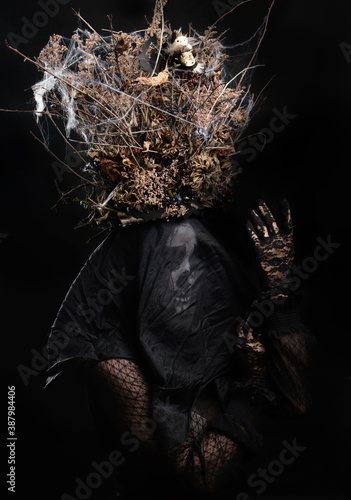woman in black clothes and skull makeup, a crown of dry branches and flowers on her head
