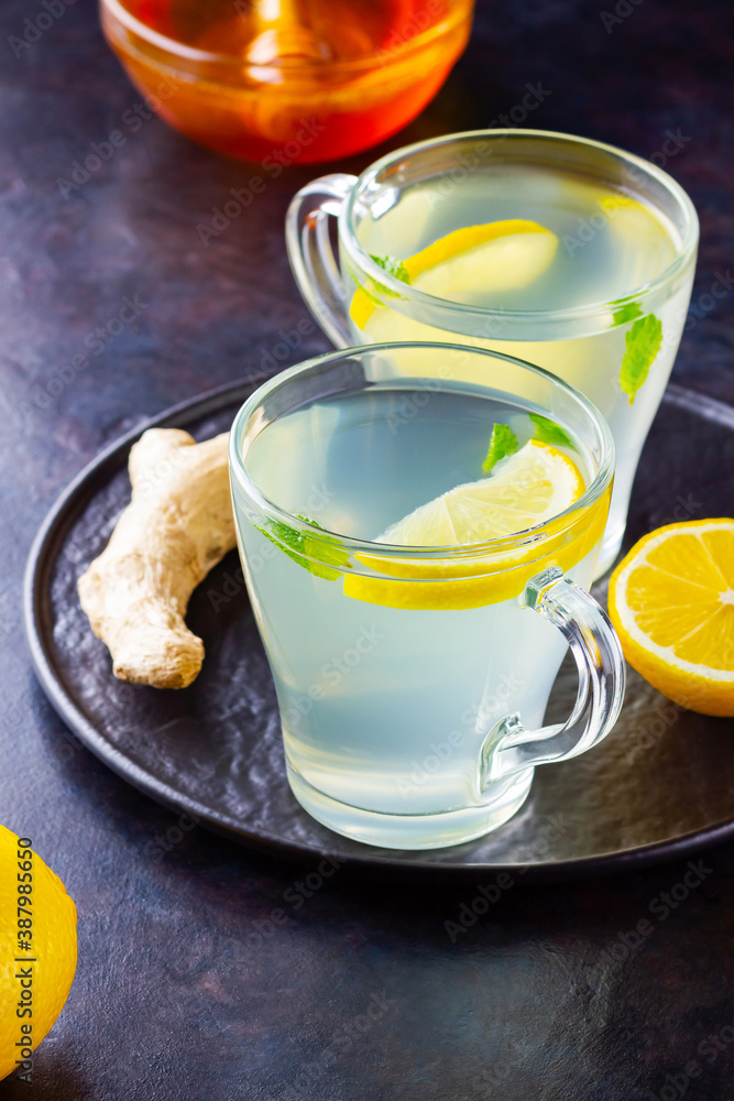 Ginger tea with lemon on a dark background. Two cups of ginger tea on a black plate