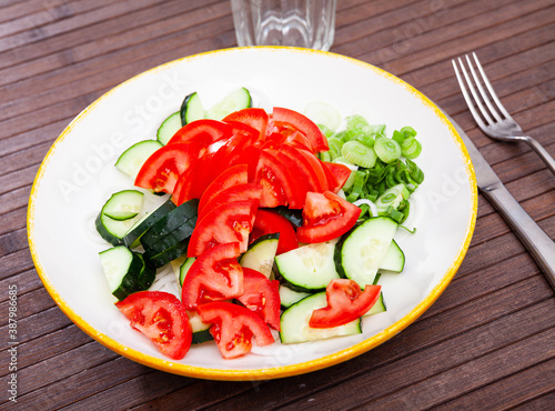 Traditional summer salad from fresh ripe tomatoes with cucumbers and green onions dressed with oil. Vegetarian appetizer
