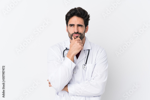 Young handsome man with beard over isolated white background wearing a doctor gown and thinking