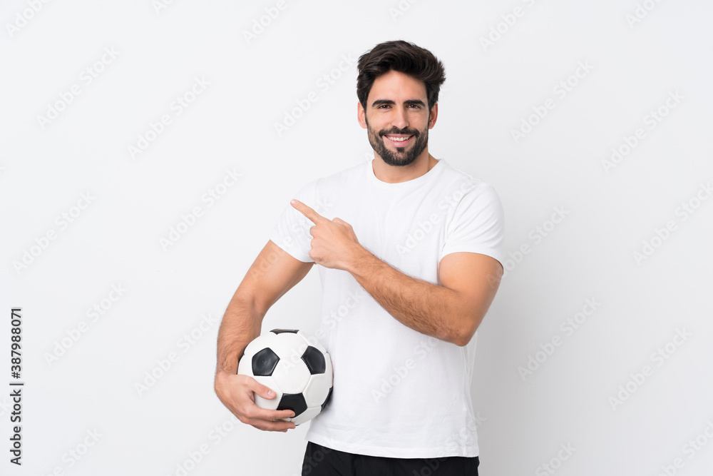 Young handsome man with beard over isolated white background with soccer ball and pointing to the lateral Young handsome man with beard over isolated white background with soccer ball and pointing to the lateral
