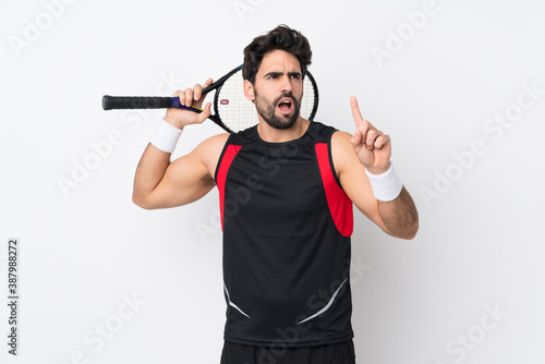 Young handsome man with beard over isolated white background playing tennis and pointing up