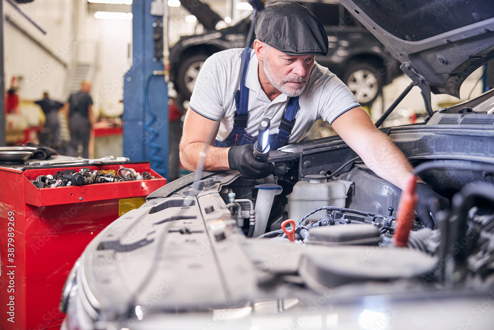 Bearded auto mechanic fixing car engine at service station Bearded auto mechanic fixing car engine at service station