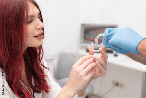 Doctor orthodontist shows a woman silicone aligners to straighten teeth photo