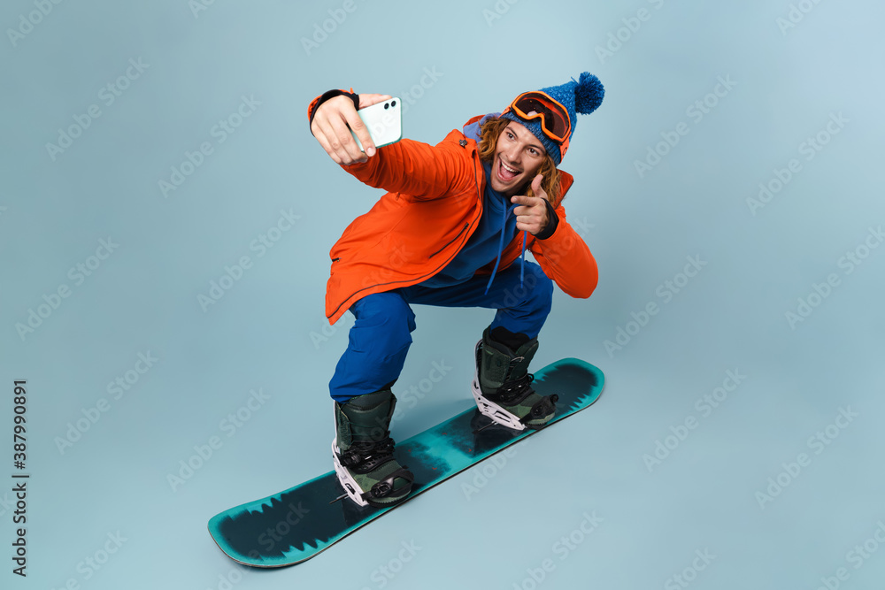 Handsome happy sportsman taking selfie on cellphone while snowboarding Handsome happy sportsman taking selfie on cellphone while snowboarding