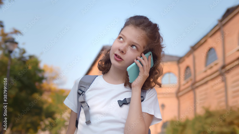 Teenage schoolgirl talking on phone and smiling standing outdoors Teenage schoolgirl talking on phone and smiling standing outdoors