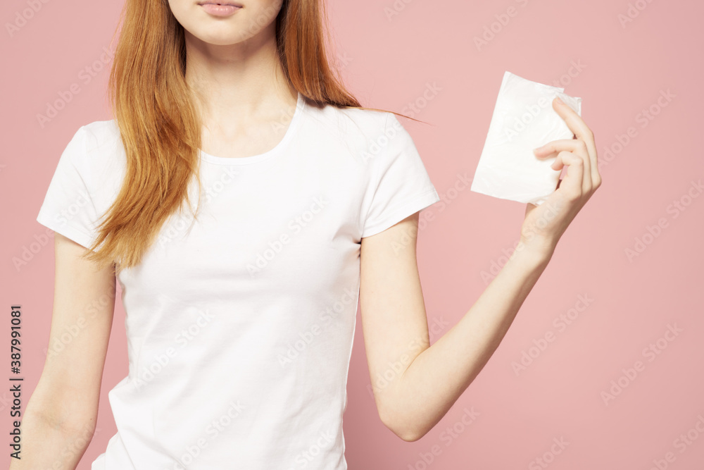 Red-haired woman with a pad in her hand and in a white T-shirt on a pink background hygiene care for the appearance