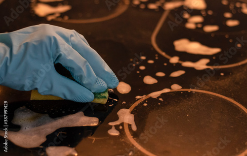 
Hand in a blue rubber glove holds a cleaning sponge and wipes off soap suds on a black background photo