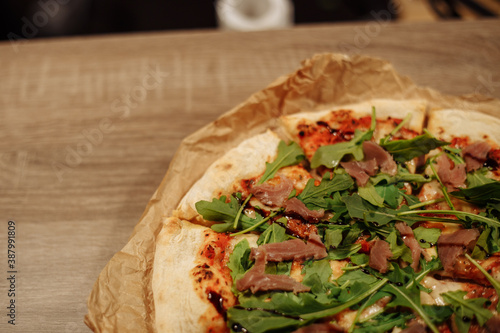 fresh pizza with herbs, tuna and balsamic sauce on food paper on a wooden table in a cozy cafe