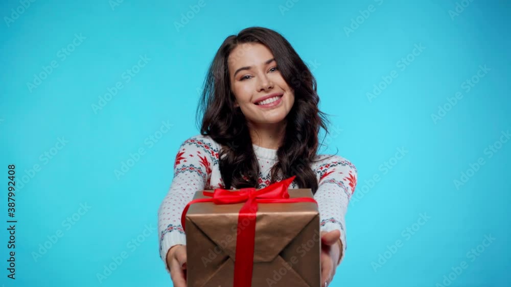 Happy young adult woman showing gift box, while looking at camera on blue Happy young adult woman showing gift box, while looking at camera on blue