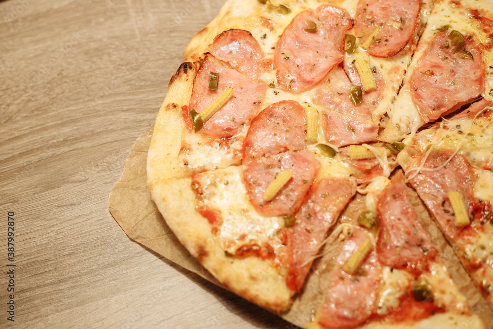pizza with sausage, mini corn, jalapeno pepper on food paper on a wooden table in warm light pizza with sausage, mini corn, jalapeno pepper on food paper on a wooden table in warm light