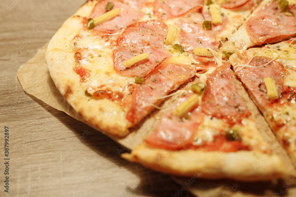 pizza with sausage, mini corn, jalapeno pepper on food paper on a wooden table in warm light pizza with sausage, mini corn, jalapeno pepper on food paper on a wooden table in warm light