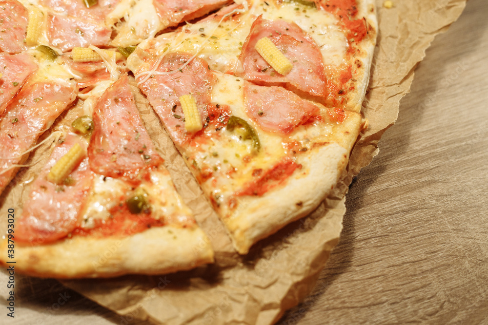 pizza with sausage, mini corn, jalapeno pepper on food paper on a wooden table in warm light
