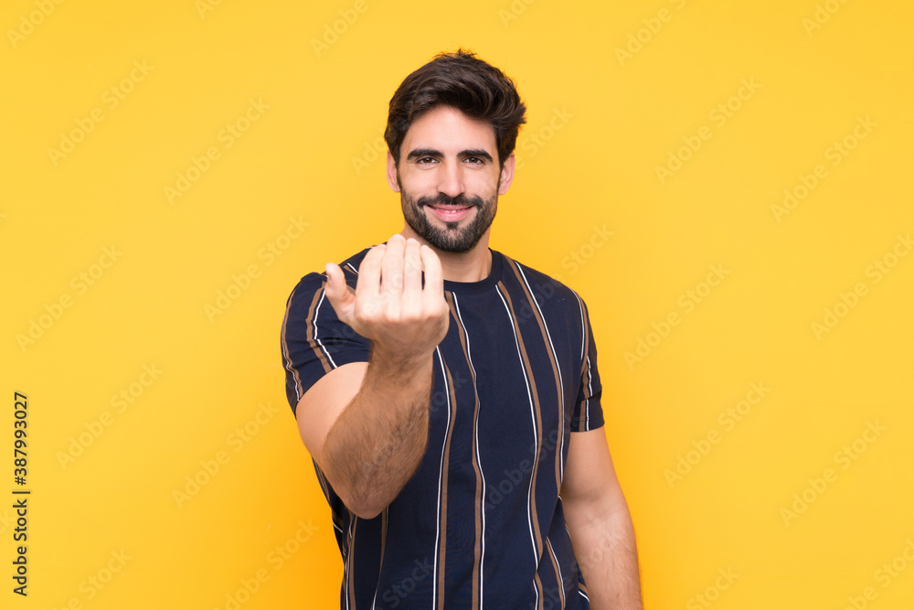 Young handsome man with beard over isolated yellow background inviting to come Young handsome man with beard over isolated yellow background inviting to come
