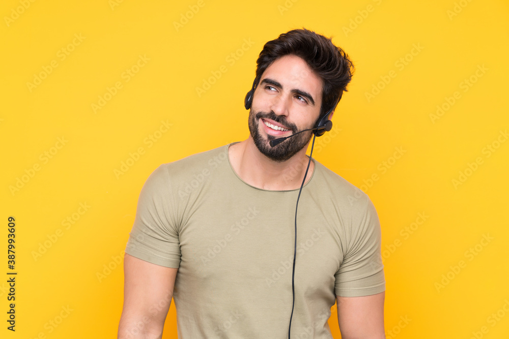 Telemarketer man working with a headset over isolated yellow background laughing and looking up Telemarketer man working with a headset over isolated yellow background laughing and looking up