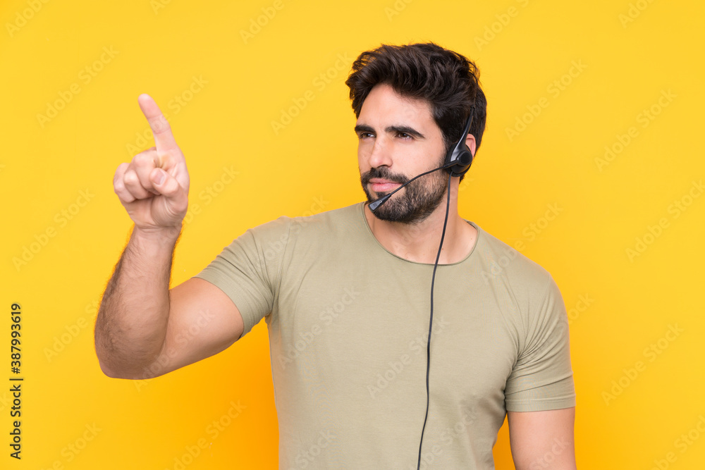 Fototapeta premium Telemarketer man working with a headset over isolated yellow background touching on transparent screen