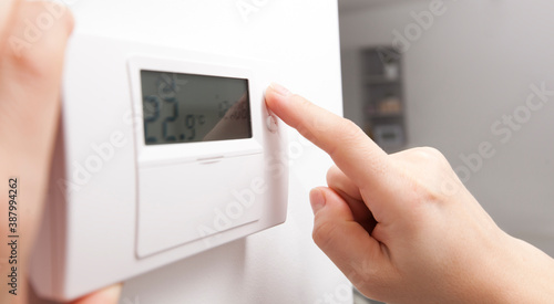 The woman adjusts the thermostat in the house