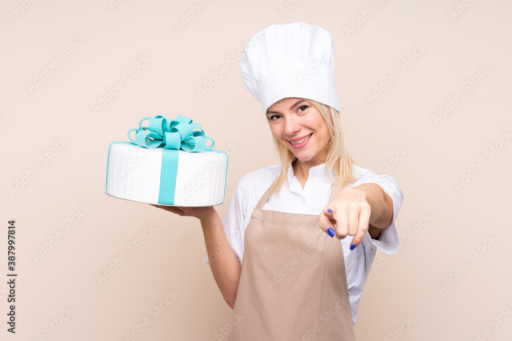 Young Russian woman with a big cake over isolated background points finger at you with a confident expression Young Russian woman with a big cake over isolated background points finger at you with a confident expression