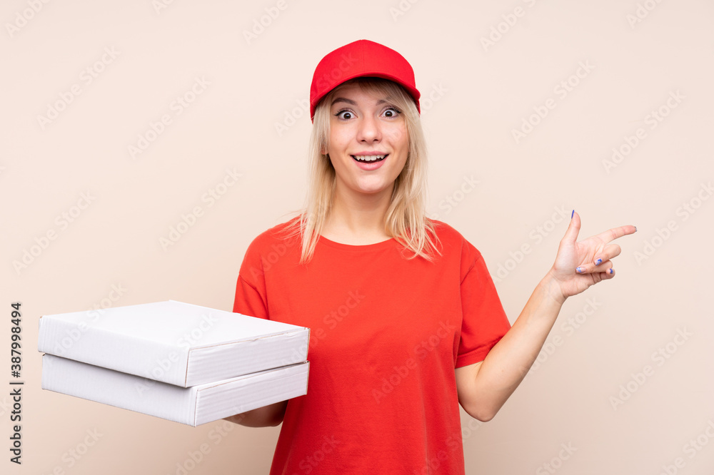Pizza delivery Russian woman holding a pizza over isolated wall surprised and pointing finger to the side Pizza delivery Russian woman holding a pizza over isolated wall surprised and pointing finger to the side