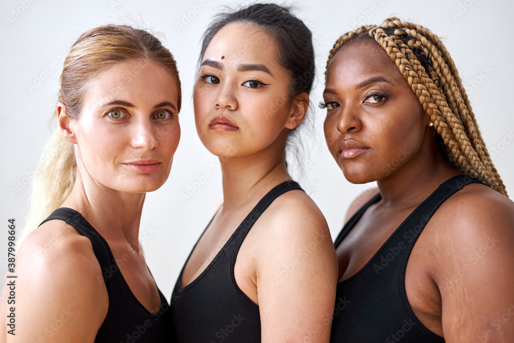 three young diverse multi ethnic female models of different race, hair  colour and body size posing at camera, friendly females in black  sportswear. tolerance and natural beauty concept Stock Photo