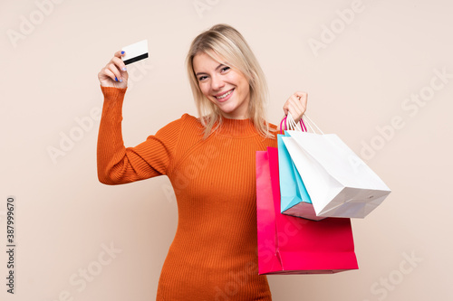 Young blonde woman over isolated background holding shopping bags and a credit card